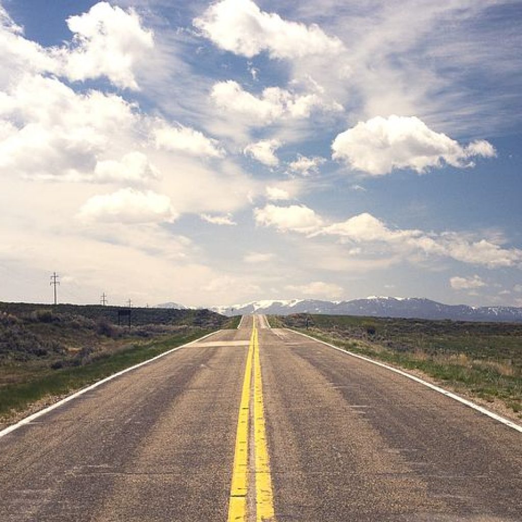 Photograph of long road vanishing in the distance, with blue skies overhead.